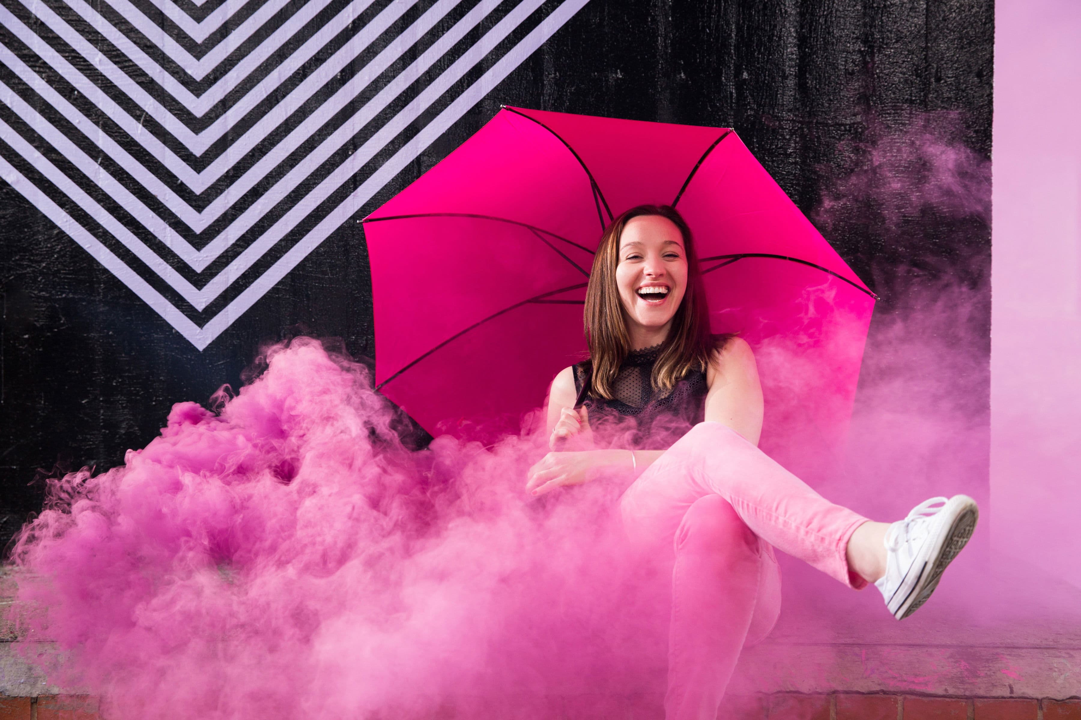Cordelia Kate laughing under a pink umbrella, surrounded by pink smoke